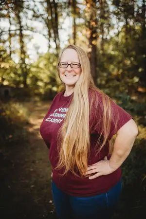 A woman standing in the woods wearing glasses.