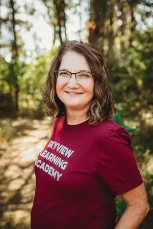 A woman in glasses and a red shirt is smiling.