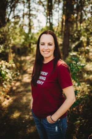 A woman standing in the woods wearing a red shirt.