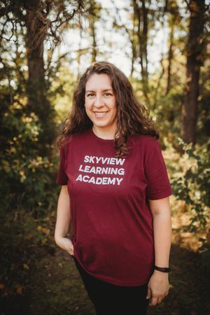 A woman in maroon shirt standing next to trees.